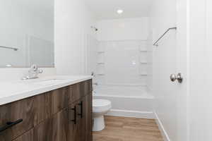 Bathroom featuring toilet, vanity,  shower combination, and wood finished floors