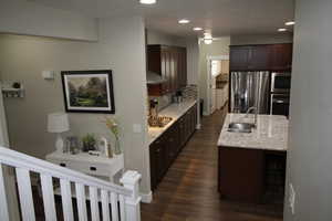 Kitchen featuring dark wood-type flooring, decorative backsplash, a sink, dark brown cabinetry, and appliances with stainless steel finishes