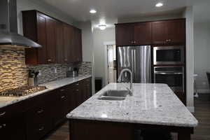 Kitchen with tasteful backsplash, dark wood finished floors, a sink, wall chimney range hood, and appliances with stainless steel finishes