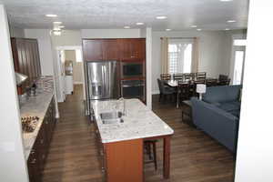 Kitchen featuring an island with sink, a breakfast bar, appliances with stainless steel finishes, and dark wood-style floors