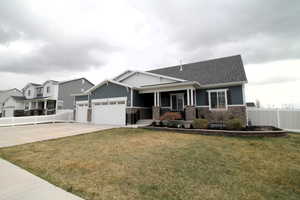 Craftsman-style house featuring concrete driveway, fence, an attached garage, stone siding, and a front lawn