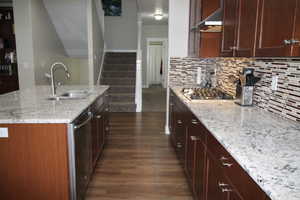 Kitchen featuring light granite counters, range hood, a sink, appliances with stainless steel finishes, and dark wood-style flooring