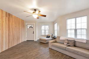 Living room featuring wooden walls, ceiling fan, and dark wood-style flooring