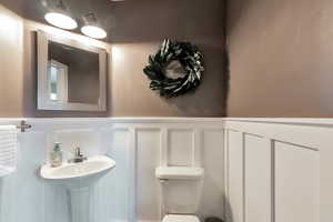 Half bath with a decorative wall, a wainscoted wall, and toilet