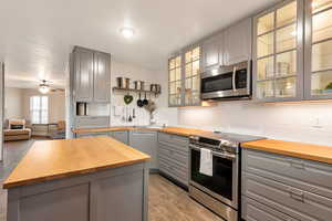 Kitchen with wooden counters, stainless steel appliances, backsplash, gray cabinets, and a kitchen island