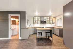Kitchen with wood finished floors, appliances with stainless steel finishes, a center island, gray cabinetry, and glass insert cabinets
