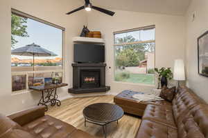 Living area with vaulted ceiling, visible vents, a ceiling fan, a glass covered fireplace, and wood finished floors
