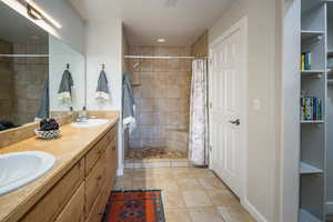 Full bathroom with double vanity, a sink, and tiled shower