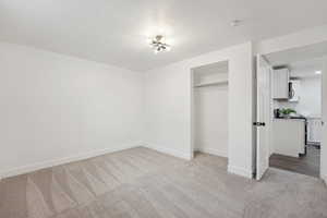 Unfurnished bedroom with light colored carpet, a closet, baseboards, and a textured ceiling