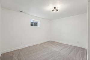 Spare room with a textured ceiling, baseboards, light colored carpet, visible vents, and an inviting chandelier