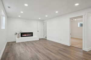 Unfurnished living room featuring wood finished floors, a glass covered fireplace, baseboards, visible vents, and recessed lighting
