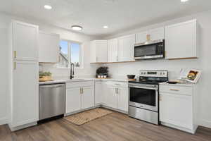 Kitchen with white cabinetry, a sink, wood finished floors, and appliances with stainless steel finishes