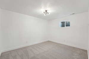 Unfurnished room featuring visible vents, light carpet, baseboards, and a textured ceiling