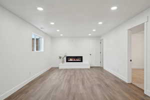 Unfurnished living room with baseboards, recessed lighting, wood finished floors, and a glass covered fireplace