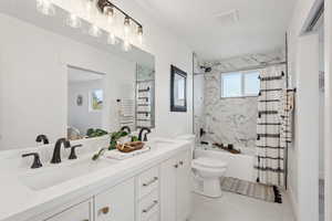 Full bathroom with double vanity, toilet, shower / tub combo with curtain, and a sink