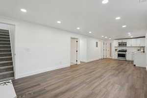 Unfurnished living room with stairs, recessed lighting, wood finished floors, and a sink