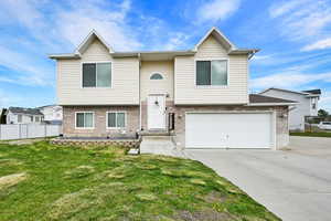 Raised ranch featuring a front yard, concrete driveway, an attached garage, fence, and brick siding