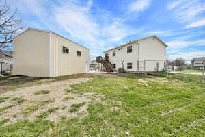 Back of house with central air condition unit, fence, stairway, an outbuilding, and a yard