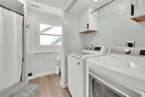Clothes washing area with washing machine and clothes dryer, visible vents, light wood finished floors, baseboards, and laundry area