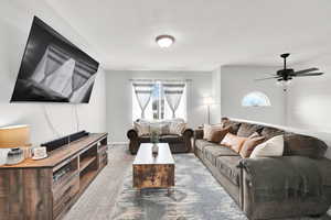 Living room with carpet, baseboards, a textured ceiling, and ceiling fan