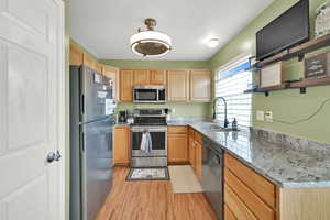 Kitchen with light wood finished floors, appliances with stainless steel finishes, a sink, open shelves, and light brown cabinetry
