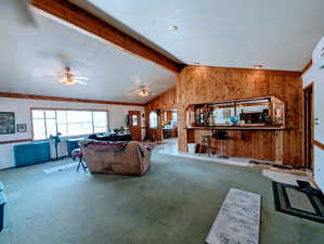 Carpeted living area with vaulted ceiling with beams, a ceiling fan, and wooden walls