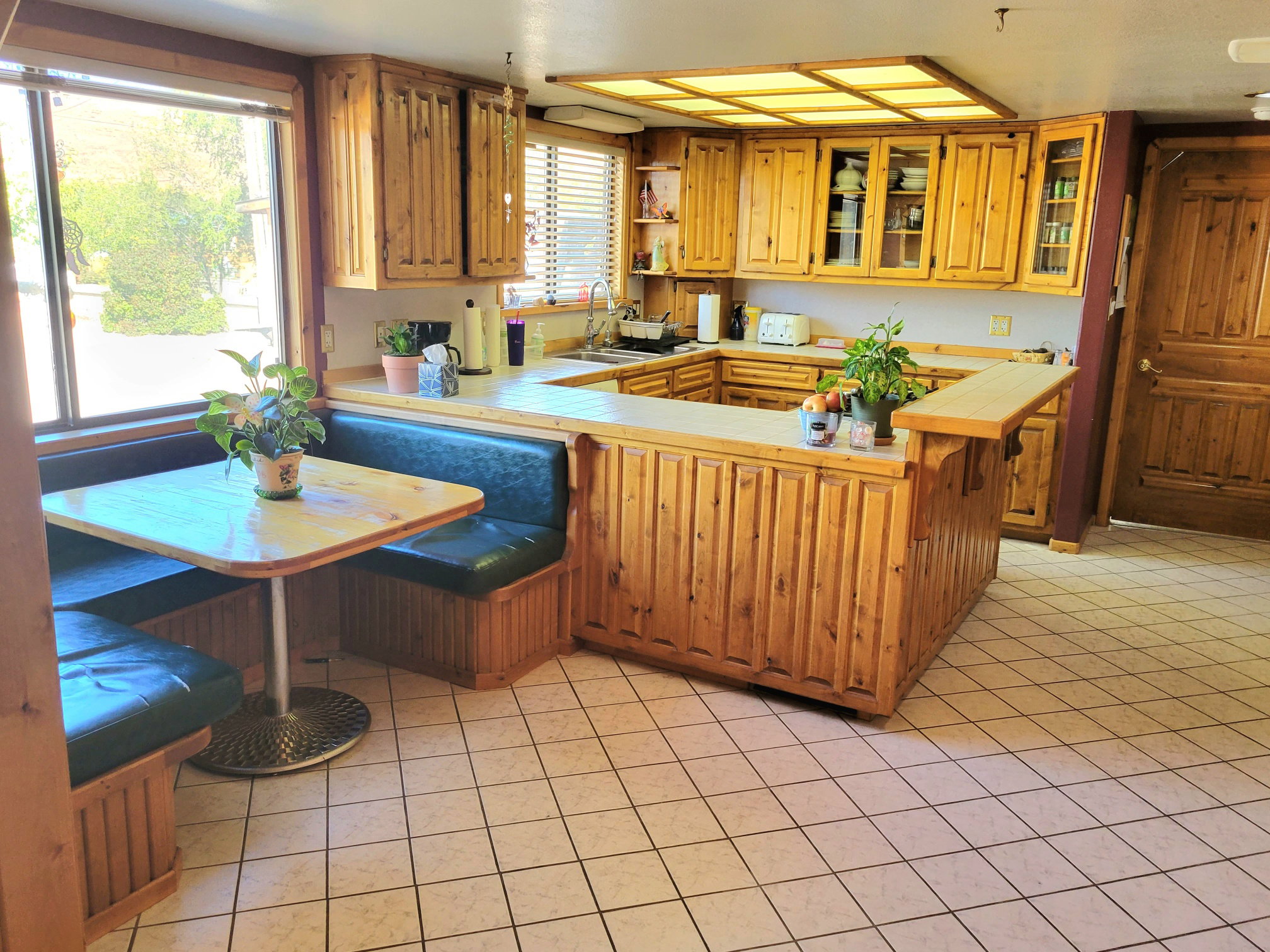 Kitchen featuring light tile patterned flooring, a sink, a peninsula, glass insert cabinets, and tile countertops