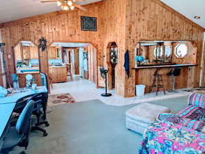 Vaulted ceiling, wooden walls, ceiling fan, and carpet