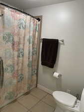 Full bathroom with a shower with curtain, baseboards, toilet, and tile patterned flooring