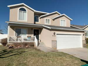 Traditional-style house featuring a front yard, a garage, a porch, and stucco siding