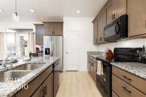 Kitchen featuring a sink, granite countertops, hanging light fixtures, black appliances, and light wood-style floors