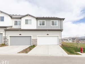 View of property featuring stone siding, 2 car garage, central AC, concrete driveway, and lawn