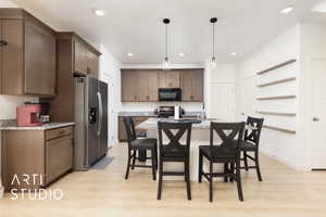 Kitchen featuring beautiful granite countertops, stainless steel fridge, range with electric stovetop, and black microwave. Light wood-type flooring, recessed lighting, and wall shelves