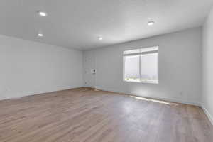 Unfurnished room with recessed lighting, baseboards, light wood finished floors, and a textured ceiling