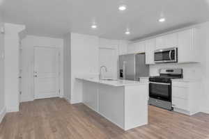 Kitchen featuring light wood finished floors, white cabinetry, a sink, and stainless steel appliances