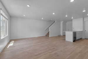 Unfurnished living room featuring visible vents, light wood finished floors, baseboards, stairs, and recessed lighting