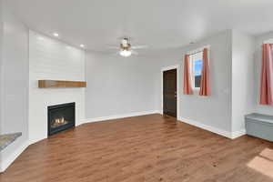 Unfurnished living room featuring a ceiling fan, wood finished floors, recessed lighting, and a large fireplace