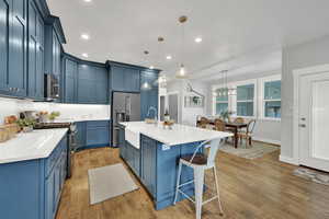 Kitchen with stainless steel appliances, blue cabinets, a breakfast bar, light wood finished floors, and decorative backsplash