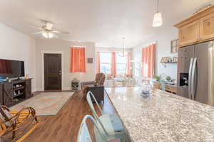 Kitchen featuring light stone counters, stainless steel fridge, open floor plan, ceiling fan with notable chandelier, and dark wood-style flooring