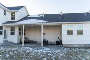 Snow covered house with a shingled roof, entry steps, and a patio area