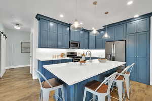 Kitchen with appliances with stainless steel finishes, blue cabinetry, light wood-style flooring, light countertops, and a kitchen bar