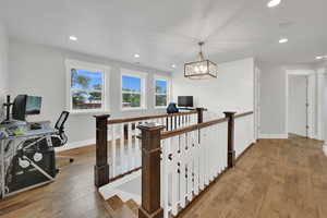 Hallway with an upstairs landing, light wood-style flooring, a desk, recessed lighting, and a chandelier