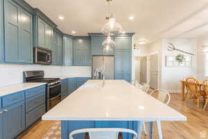 Kitchen featuring tasteful backsplash, appliances with stainless steel finishes, a sink, light wood-style floors, and a kitchen breakfast bar