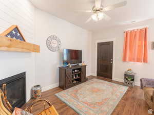 Living room featuring a large fireplace, visible vents, baseboards, wood finished floors, and a ceiling fan