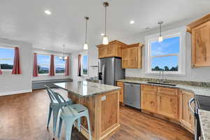 Kitchen featuring appliances with stainless steel finishes, a kitchen island, light wood finished floors, light stone countertops, and recessed lighting