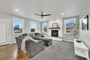 Living room with ceiling fan, a large fireplace, recessed lighting, and wood finished floors