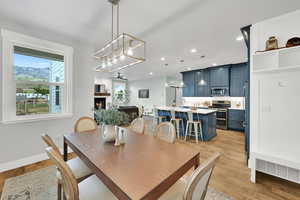 Dining room with a chandelier, light wood-style flooring, a warm lit fireplace, and recessed lighting