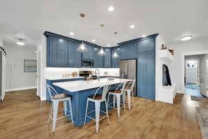 Kitchen with appliances with stainless steel finishes, blue cabinetry, light countertops, a kitchen breakfast bar, and light wood-type flooring