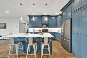 Kitchen with stainless steel appliances, a barn door, a breakfast bar, light wood-type flooring, and recessed lighting