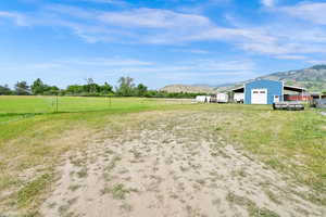 View of yard featuring a garage, a mountain view, an outdoor structure, a view of countryside, and driveway